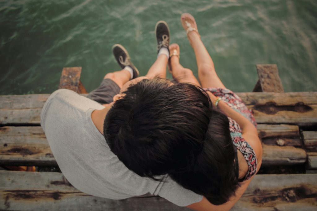 a young couple sitting on a dock holding hands